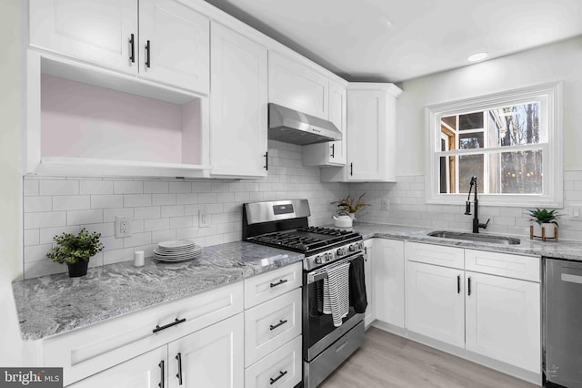 kitchen featuring sink, range hood, appliances with stainless steel finishes, light stone counters, and white cabinetry