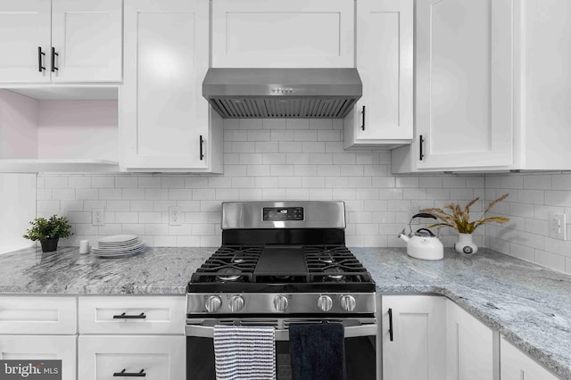 kitchen with decorative backsplash, light stone countertops, wall chimney exhaust hood, gas stove, and white cabinets