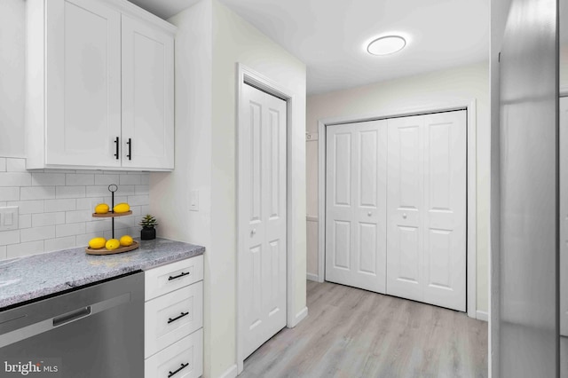 kitchen featuring white cabinets, light hardwood / wood-style flooring, stainless steel dishwasher, decorative backsplash, and light stone counters