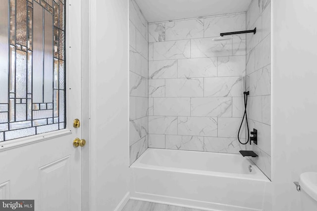 bathroom featuring hardwood / wood-style floors, tiled shower / bath combo, and toilet