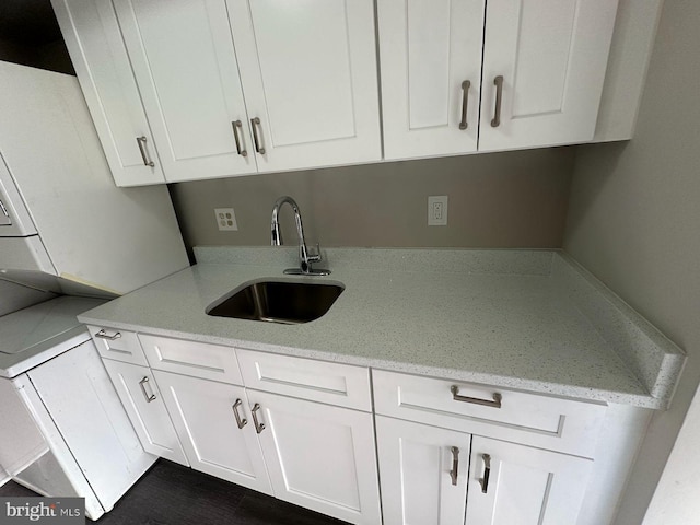 kitchen with light stone counters, white cabinetry, and sink