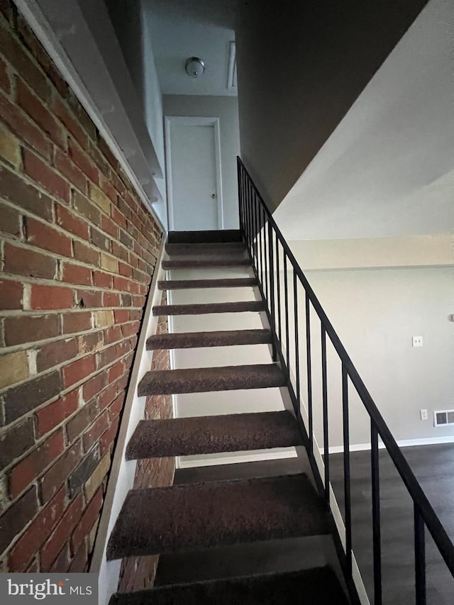 stairway with hardwood / wood-style flooring and brick wall