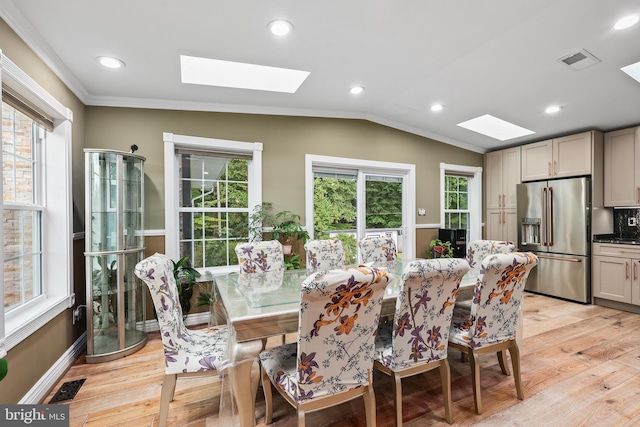 dining area featuring light hardwood / wood-style floors, a wealth of natural light, crown molding, and vaulted ceiling with skylight