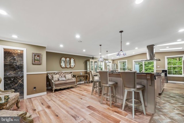 kitchen featuring a kitchen bar, island range hood, hanging light fixtures, and light wood-type flooring