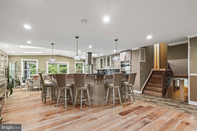 kitchen with island range hood, lofted ceiling with skylight, double oven, light hardwood / wood-style floors, and a breakfast bar area