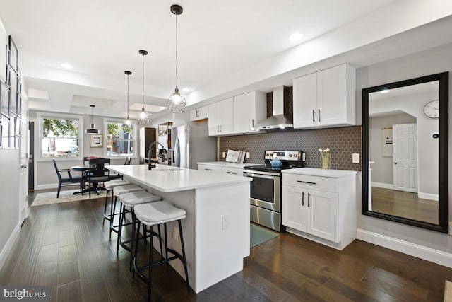 kitchen featuring wall chimney exhaust hood, decorative light fixtures, a center island with sink, white cabinets, and appliances with stainless steel finishes