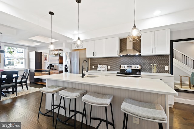 kitchen with sink, wall chimney exhaust hood, a kitchen island with sink, white cabinets, and appliances with stainless steel finishes