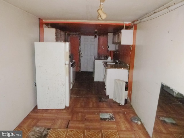 kitchen featuring radiator, dark parquet floors, white fridge, washer / dryer, and white cabinets