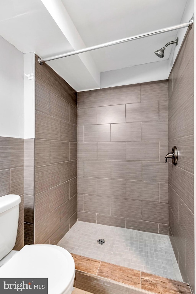 bathroom with toilet, tiled shower, and tile walls