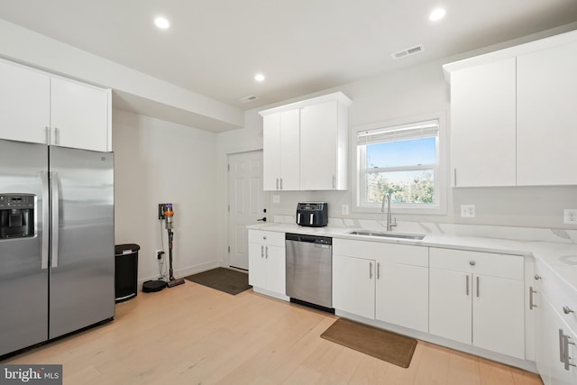 kitchen featuring visible vents, white cabinets, stainless steel appliances, light countertops, and a sink