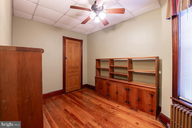 interior space with hardwood / wood-style floors, a drop ceiling, ceiling fan, and radiator heating unit