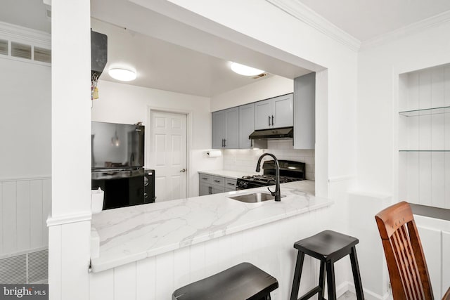 kitchen with gray cabinetry, black appliances, crown molding, light stone countertops, and a kitchen bar