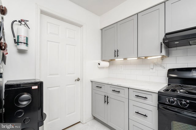 kitchen featuring decorative backsplash, light stone countertops, wall chimney exhaust hood, gray cabinetry, and gas stove