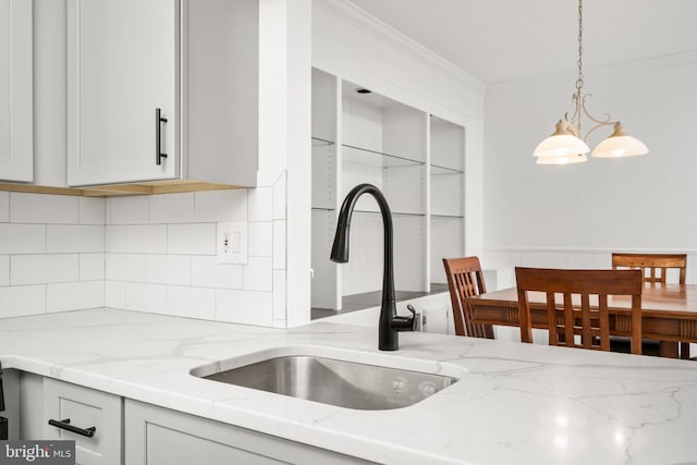 kitchen with sink, a notable chandelier, light stone counters, and crown molding