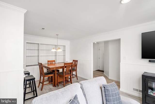 dining area with crown molding, a chandelier, and light wood-type flooring