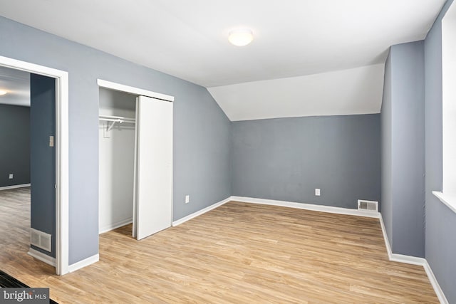 unfurnished bedroom with vaulted ceiling, a closet, and light hardwood / wood-style flooring