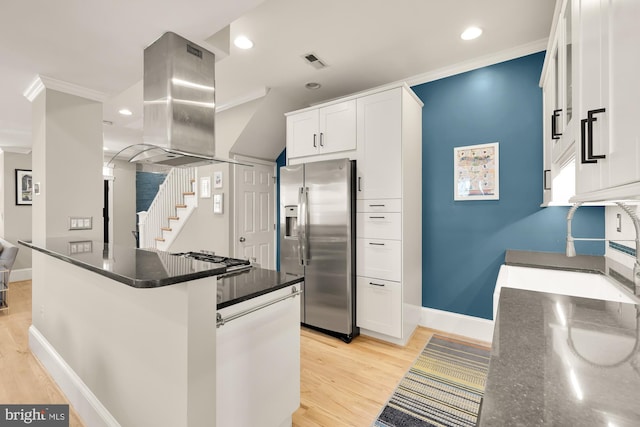 kitchen with crown molding, dark stone counters, island range hood, white cabinets, and appliances with stainless steel finishes