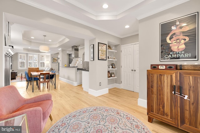 interior space featuring a raised ceiling, crown molding, built in features, and light hardwood / wood-style floors