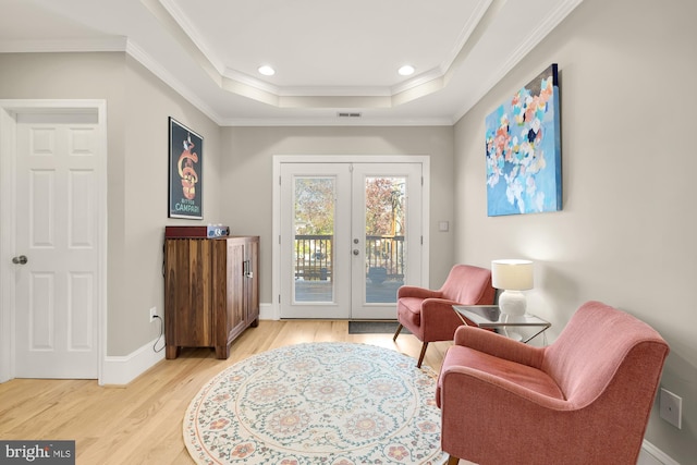 sitting room with french doors, a tray ceiling, crown molding, and light hardwood / wood-style floors