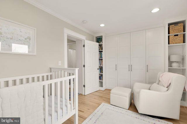 bedroom with hardwood / wood-style floors, a closet, a nursery area, and crown molding