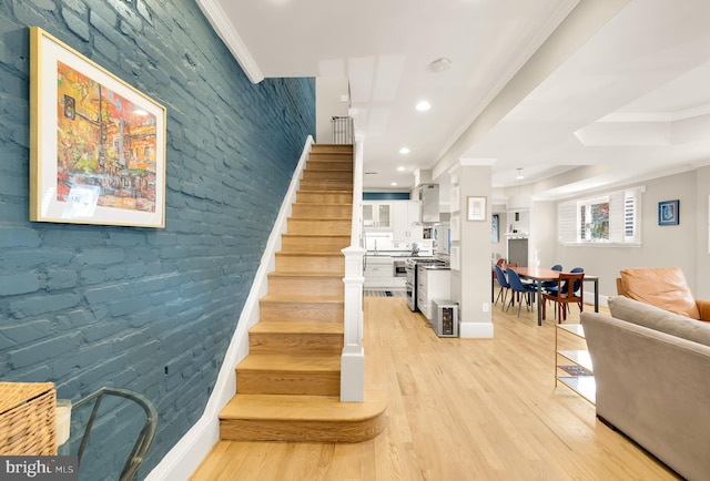 staircase featuring hardwood / wood-style floors, ornamental molding, and brick wall