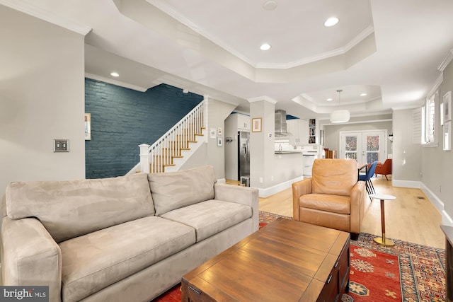 living room featuring a tray ceiling, french doors, light wood-type flooring, and ornamental molding