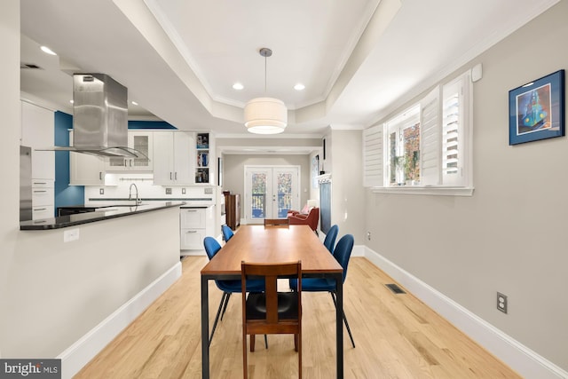 dining room with french doors, a raised ceiling, sink, ornamental molding, and light hardwood / wood-style floors