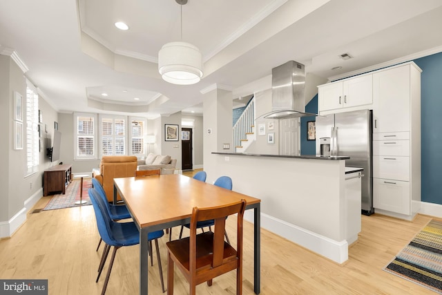 dining room featuring a raised ceiling, ornamental molding, and light wood-type flooring