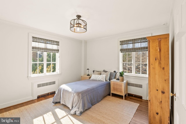 bedroom with ornamental molding, radiator heating unit, wood finished floors, and baseboards