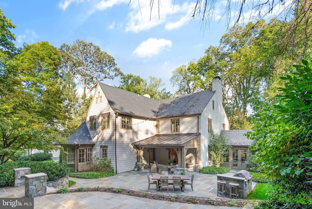 back of house featuring a patio, metal roof, french doors, a standing seam roof, and a chimney