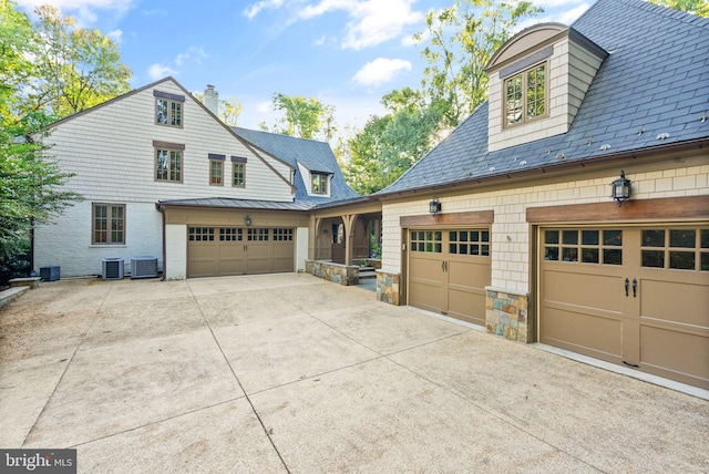 view of side of property featuring stone siding, a standing seam roof, cooling unit, and concrete driveway