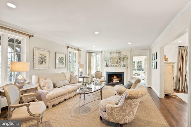 living room with recessed lighting, crown molding, a lit fireplace, and wood finished floors