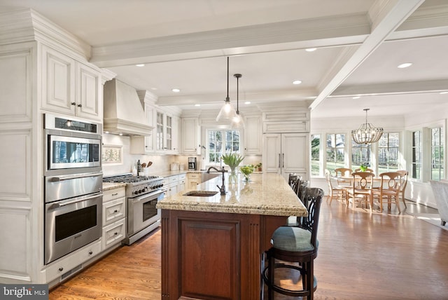 kitchen featuring light stone counters, premium range hood, a sink, light wood-style floors, and high end stainless steel range oven