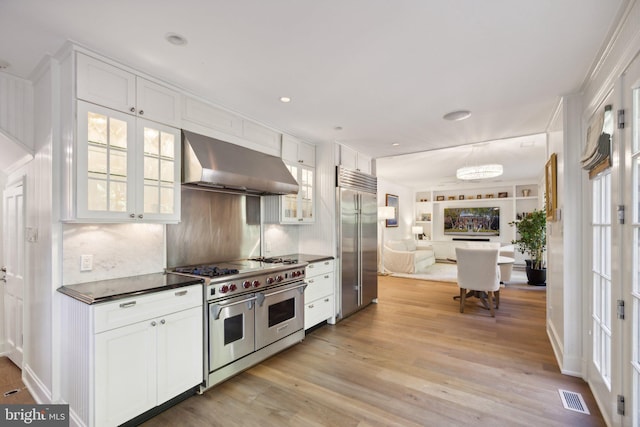 kitchen with light wood-type flooring, wall chimney exhaust hood, premium appliances, and white cabinets