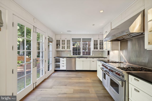 kitchen featuring tasteful backsplash, wall chimney range hood, light hardwood / wood-style flooring, appliances with stainless steel finishes, and white cabinets