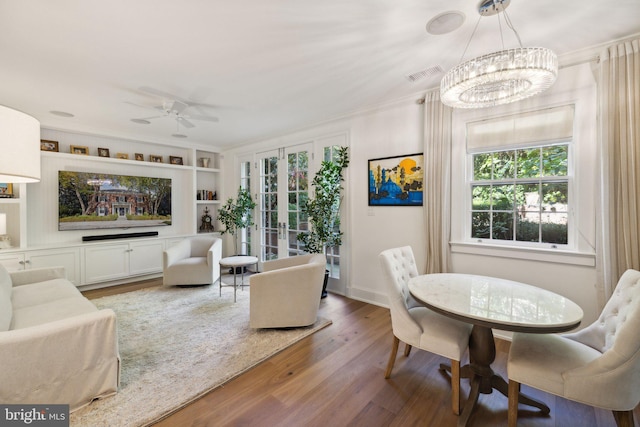 dining space with ceiling fan with notable chandelier, wood-type flooring, built in shelves, french doors, and crown molding