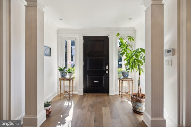 foyer entrance featuring hardwood / wood-style floors, ornamental molding, and ornate columns