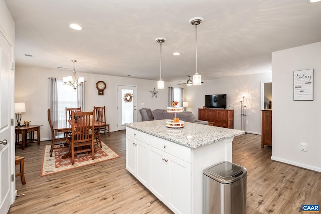 kitchen featuring light stone countertops, pendant lighting, white cabinets, light hardwood / wood-style floors, and a kitchen island