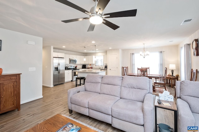 living room with light hardwood / wood-style floors and ceiling fan with notable chandelier