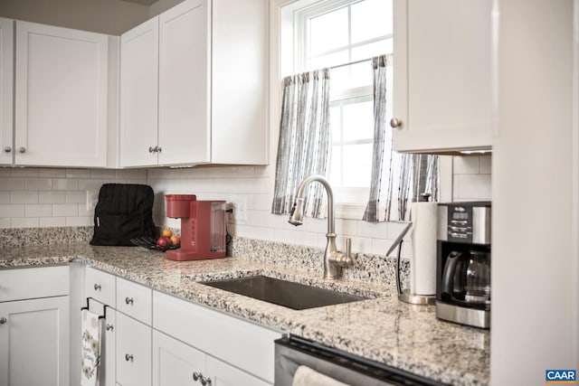 kitchen featuring white cabinets, decorative backsplash, light stone counters, and sink