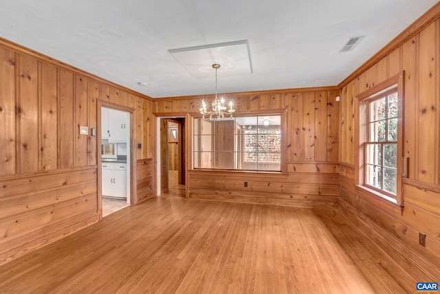 unfurnished dining area with a chandelier, wood-type flooring, crown molding, and wooden walls