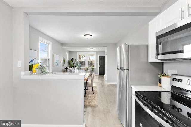 kitchen featuring electric range, light wood-type flooring, white cabinetry, and a wealth of natural light