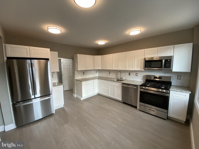 kitchen featuring decorative backsplash, appliances with stainless steel finishes, light stone counters, sink, and white cabinetry