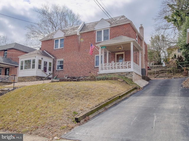 traditional home featuring a front yard, brick siding, a porch, and a chimney