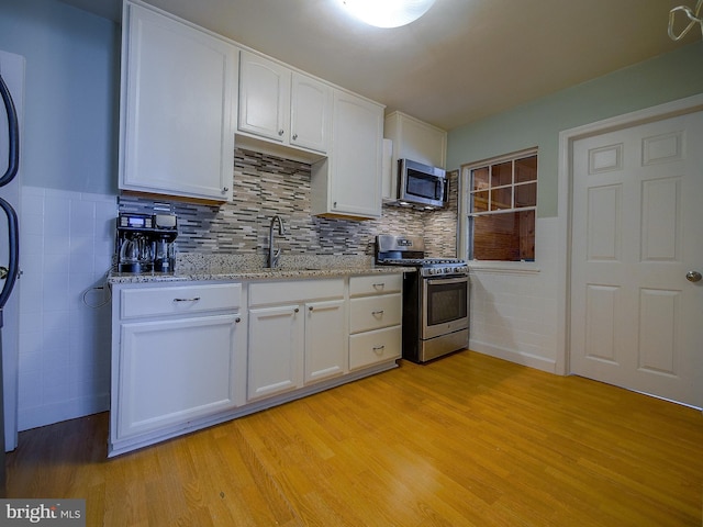 kitchen with light stone countertops, appliances with stainless steel finishes, light wood-style floors, white cabinets, and a sink