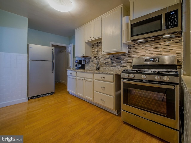 kitchen with light wood-type flooring, a sink, stainless steel appliances, white cabinets, and light stone countertops