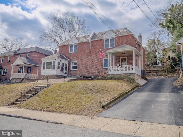 view of front of property with a front yard, driveway, a porch, a chimney, and brick siding