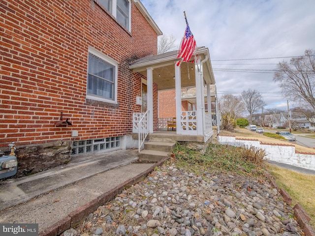 view of exterior entry featuring brick siding and a porch