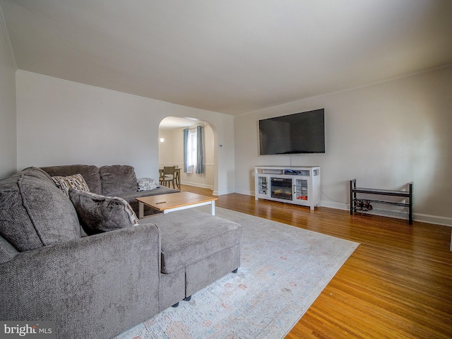 living room featuring wood finished floors, arched walkways, and baseboards