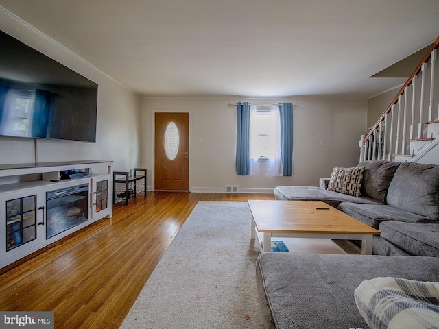 living room featuring visible vents, ornamental molding, wood finished floors, stairway, and baseboards